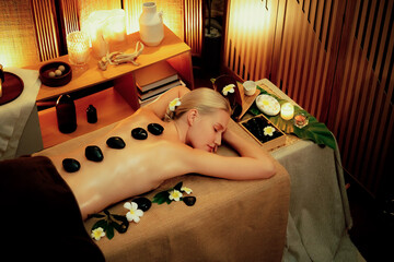 Hot stone massage at spa salon in luxury resort with warm candle light, blissful woman customer...