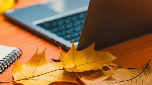 Golden autumn leaves adorn a warm wooden desk with a laptop and open notebook in the background, creating a cozy and inviting atmosphere for work or study. - Powered by Adobe