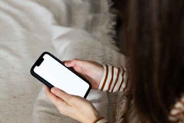 A close-up shot of a young woman sitting in her bed holding a mobile phone in her hands looking at...