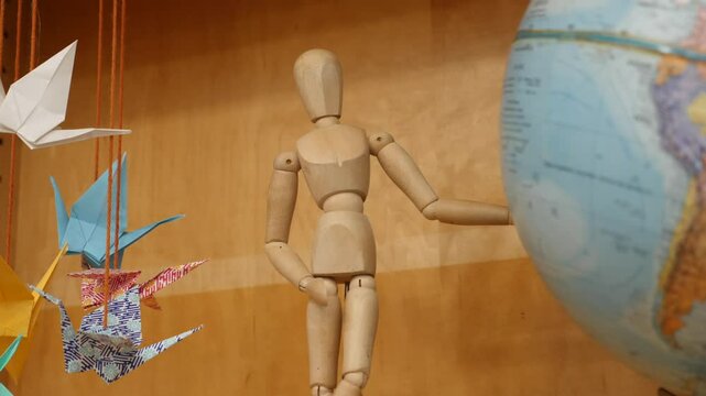 Wooden figure observes paper cranes and globe