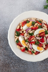 Traditional Turkish piyaz salad with white beans, eggs, tomatoes, onion and parsley. Top view, gray background.