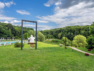 Swinging into Summer: Woman Enjoying a View of a Luxury Resort with a Pool and Forest,Rear View.Modern Recreation: Enjoying the Outdoors on a Stylish Swing at a Scenic Holiday Destination