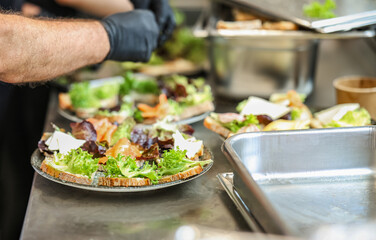 Open-faced sandwiches being prepared in a professional kitchen with fresh lettuce, cheese, and smoked salmon, illustrating modern food service and hygiene