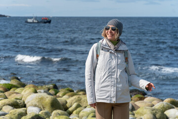 Woman smiles while standing on the distinctive rounded boulders at Dragon Eggs Beach in Teriberka,...