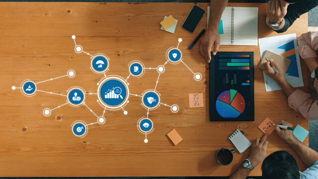 A top-down view of a collaborative meeting with professionals analyzing data visualizations and discussing project management strategies. The setup emphasizes teamwork and organization. Amity