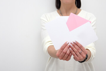 A girl in light-colored clothes holds several white and pink advertising envelopes in her hands. A flat envelope in a woman's hands with an empty space. Invitation, package, and letter