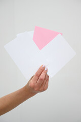 A girl in light-colored clothes holds several white and pink advertising envelopes in her hands. A flat envelope in a woman's hands with an empty space. Invitation, package, and letter