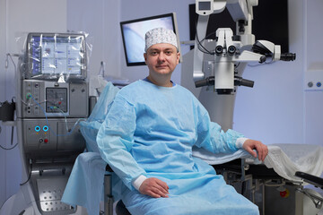 Portrait of middle aged man wearing surgical gown and cap sitting in operating room surrounded by...