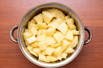 Chopped potatoes in a metal pot on a wooden surface ready for cooking in a kitchen setting