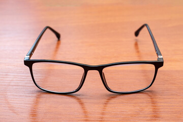 Stylish black eyeglasses resting on a wooden surface with a smooth finish in a well-lit indoor...