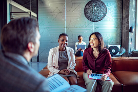 Diverse team having casual business meeting on office sofa with charts