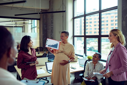 Pregnant businesswoman presenting growth chart to diverse team in office meeting