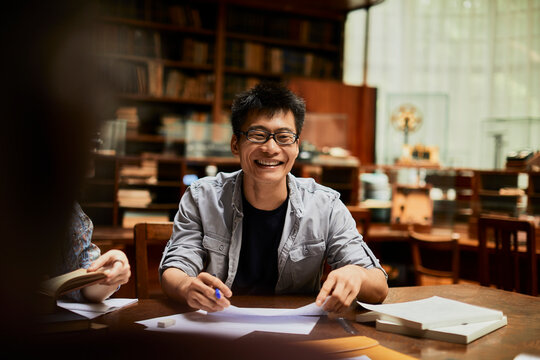 Happy student studying at library table with books and notes