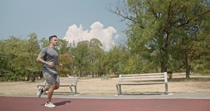 A young man runs on a track in a park. He is wearing athletic clothing and is focused on his workout. He represents fitness, health, and a determined mindset.