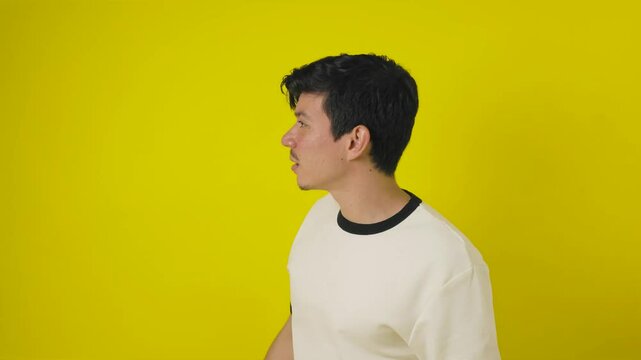 Disoriented freckled young man walks while looking around for direction on a yellow background with copy space
