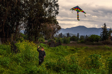 niño jugando a elevar una cometa de múltiples colores en un día nublado