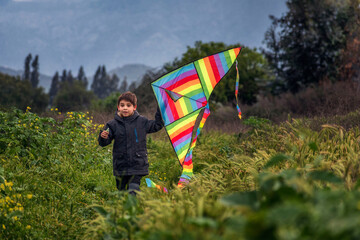 niño jugando a elevar una cometa de múltiples colores en un día nublado