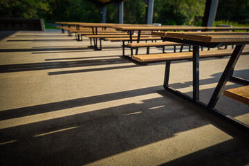 an outdoor pavilion with multiple picnic tables and benches, illuminated by natural light casting...