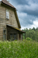 Abandoned Wooden House in Overgrown Meadow – Stormy Sky and Forgotten Countryside Building with...