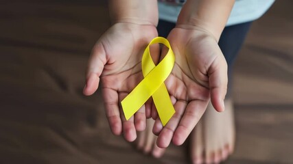 Child's hands gently holding a yellow awareness ribbon symbolizing childhood cancer or sarcoma awareness and support against, video