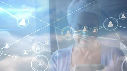 Senior woman raising tablet and tapping screen by window building cloud computing user icon network - Powered by Adobe