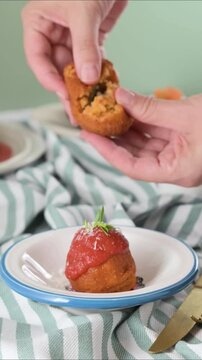 Close-up of hands breaking Sicilian arancini with rice, cheese and herbs. Crispy texture and savory filling. Traditional Italian street food. High quality FullHD footage