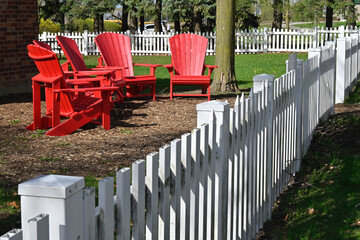 Red Adirondack chairs in the backyard with white picket fence