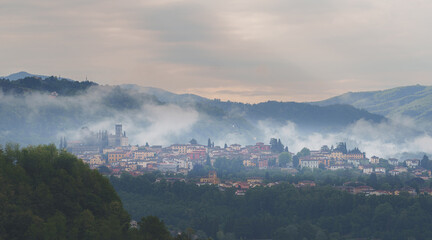 Foggy morning view of Barga village in Tuscany, Italy, surrounded by forested hills and mountains.