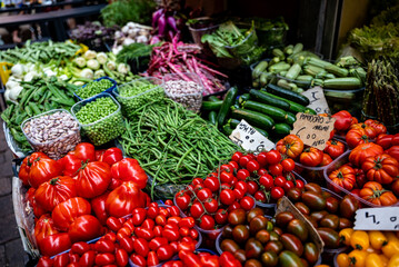 Colorful fresh vegetables and legumes are displayed at an outdoor farmers' market, including ripe tomatoes, beans, cucumbers and peas.