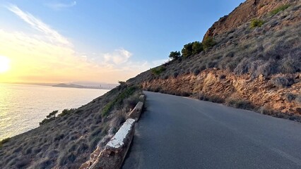 A stunningly beautiful coastal road gracefully winding along a majestic rocky hillside at sunset by the sea
