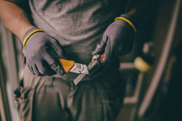 A worker holds construction knives in his hands.
