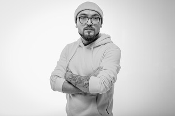 Confident man with crossed arms, wearing a beanie and glasses. Striking black and white studio...