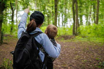 Back view of woman with backpack walking on forest trail bonding with child during outdoor adventure. Family time in nature, eco trip.