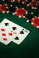 Two playing cards, an eight of hearts and an eight of spades, lie on a green felt surface with red...