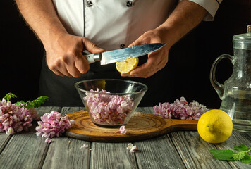 Adding lemon juice to a glass container with acacia flowers before making cold and aromatic kvass....