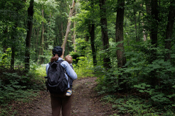 
mother with child travels through the forest with a backpack and points at birds.family travel. family concept