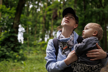 Mom holding baby while looking up in forest. Nature walk with toddler, peaceful outdoor moment, family bonding in woodland.