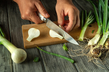 Hands skillfully cut fresh green onions on a rustic wooden board. The vibrant vegetables include...