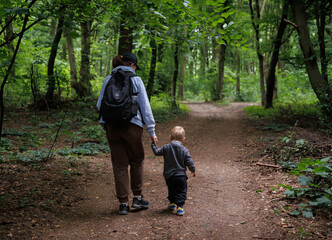 Nature walk with baby, family bonding in the forest. Mom holds baby's hand while walking along wide forest path