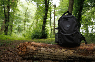 a black backpack with a bottle in its pocket stands on a stump in the forest