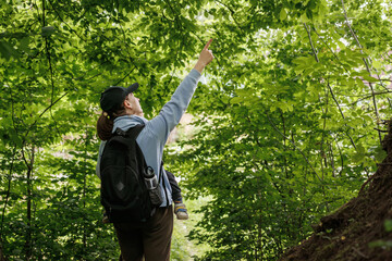 happy young man jumping in the park.Mom holding baby while looking up in forest. Nature walk with toddler, peaceful outdoor moment, family bonding in woodland.