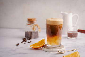 Coffee with orange juice (bumble) in a tall glass with ice on a light background with coffee beans...