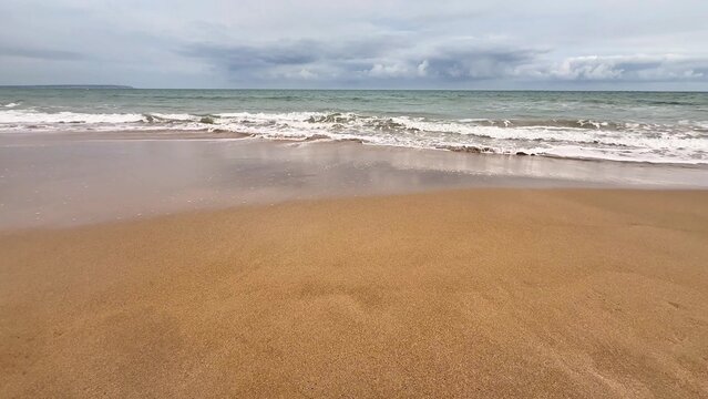 A tranquil beach scene depicting soft and warm sand, gentle waves lapping at the shore, and a cloudy horizon above