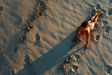 Woman practices yoga on a sandy beach at golden hour, footprints leading towards the ocean, aerial view of beach workout.