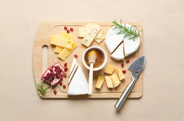 A variety of cheese, honey, pomegranate seeds and rosemary leaves on a wooden board and beige background. Top view and horizontal format.