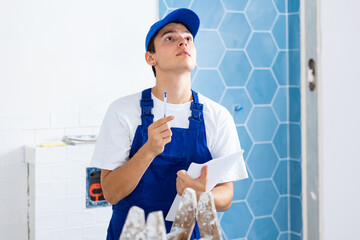 Confident young builder in blue overalls planning process of indoor building overhaul, making...