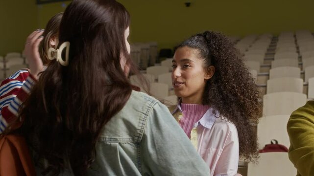 Handheld shot of multiethnic zoomers greeting each other while coming for lecture in university