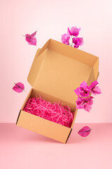Open cardboard box with bougainvillea flowers on pink background. Minimal spring advertising concept.