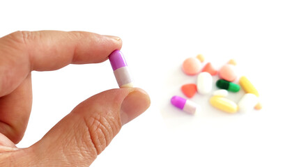 Hand holding a capsule with other pills in the background