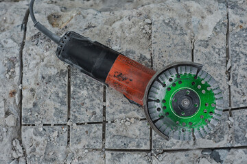 Close-up of an angle grinder with a green segmented diamond cutting disc placed on rough concrete...